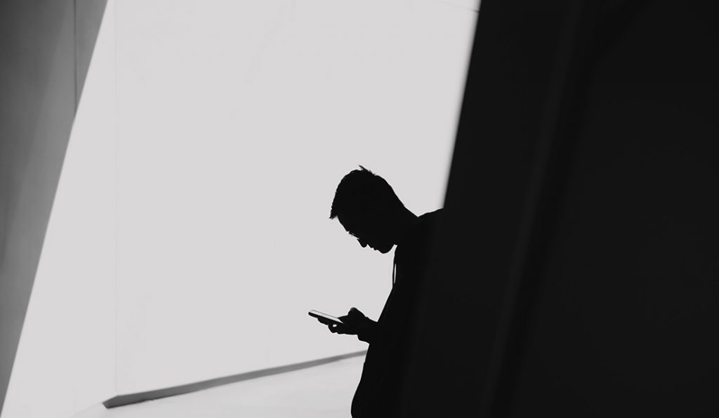 Black and white photo of silhouette of a man checking his cell phone.