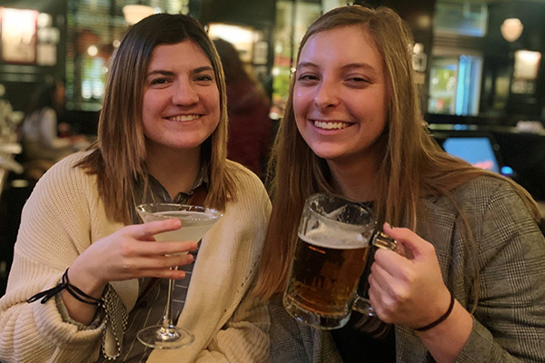 two female students clanking alcoholic beverages in a pub